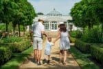 A family with a child standing happily in front of their modern white home with lush greenery, representing one of the best family neighborhoods in Dubai.