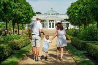A family with a child standing happily in front of their modern white home with lush greenery, representing one of the best family neighborhoods in Dubai.