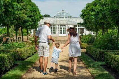 A family with a child standing happily in front of their modern white home with lush greenery, representing one of the best family neighborhoods in Dubai.