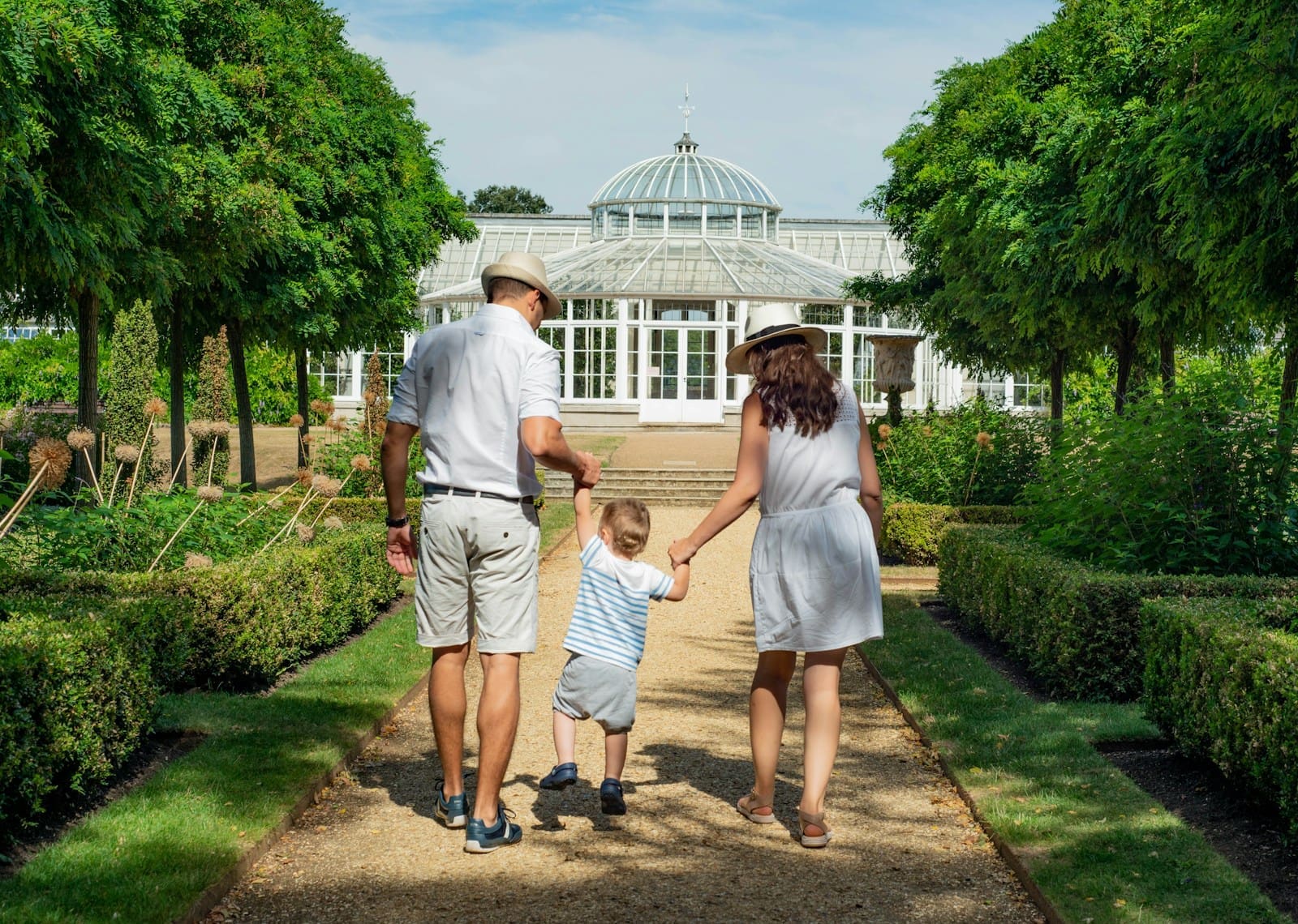 A family with a child standing happily in front of their modern white home with lush greenery, representing one of the best family neighborhoods in Dubai.