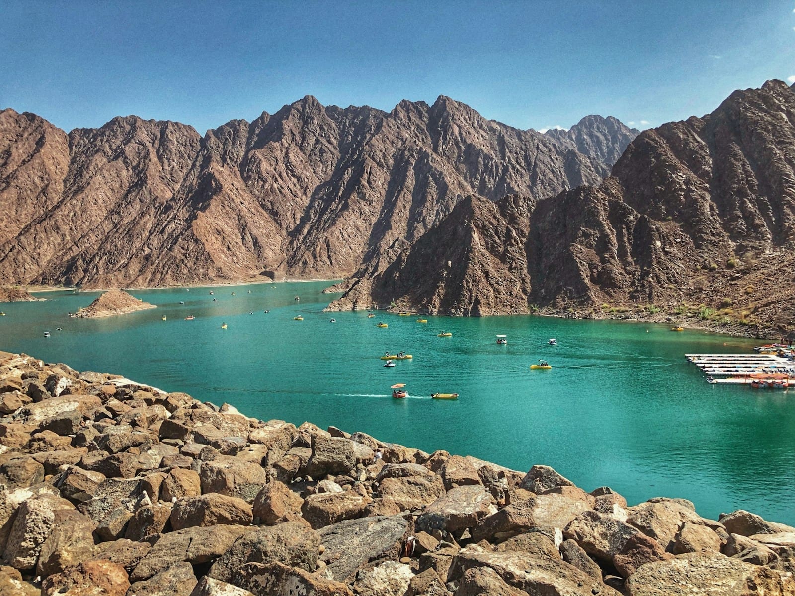 A panoramic view of the Hatta Dam, surrounded by rocky mountains under a clear blue sky.